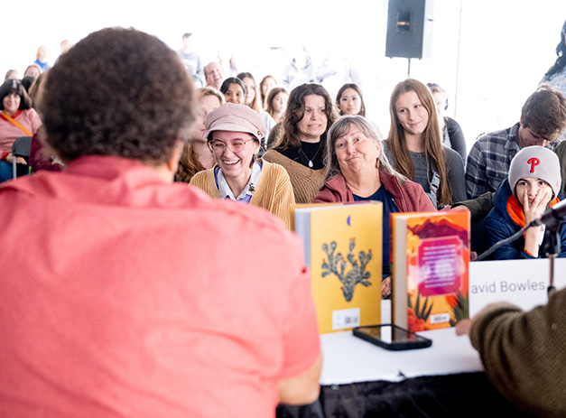 Audience members smiling and listening to an author speak at the Texas Book Festival, with books displayed on the table in front of them.