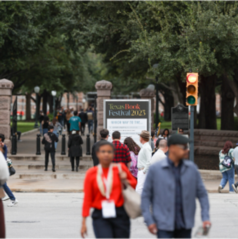 People cross the street outside the Texas Capitol with a Texas Book Festival 2023 banner in the background